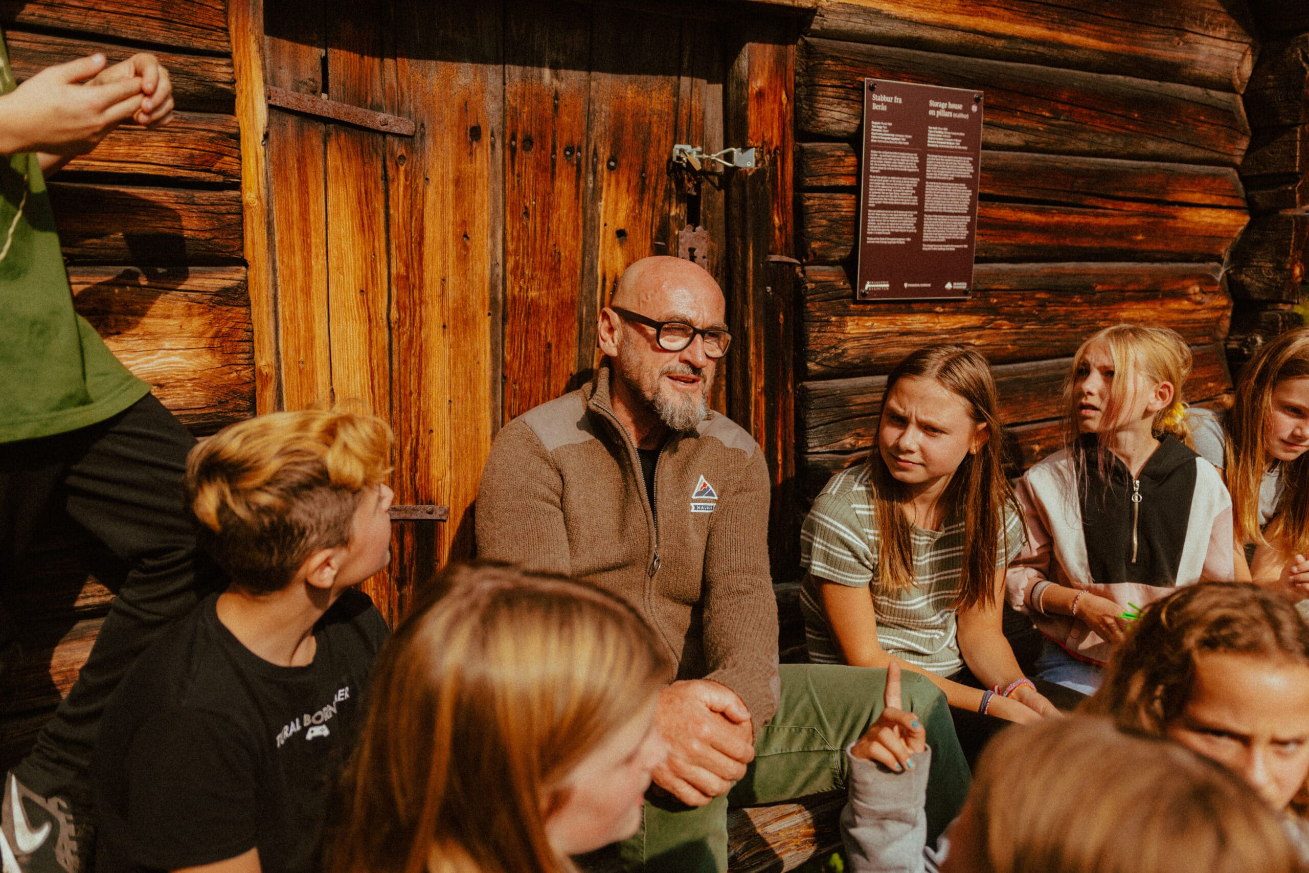Jochen Schweizer erzählt Kindern und Jugendlichen vor einer Blockhütte von seinen Erfahrungen